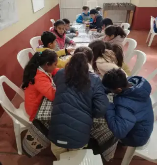 Niños trabajando en sus hojas alrededor de una mesa larga.