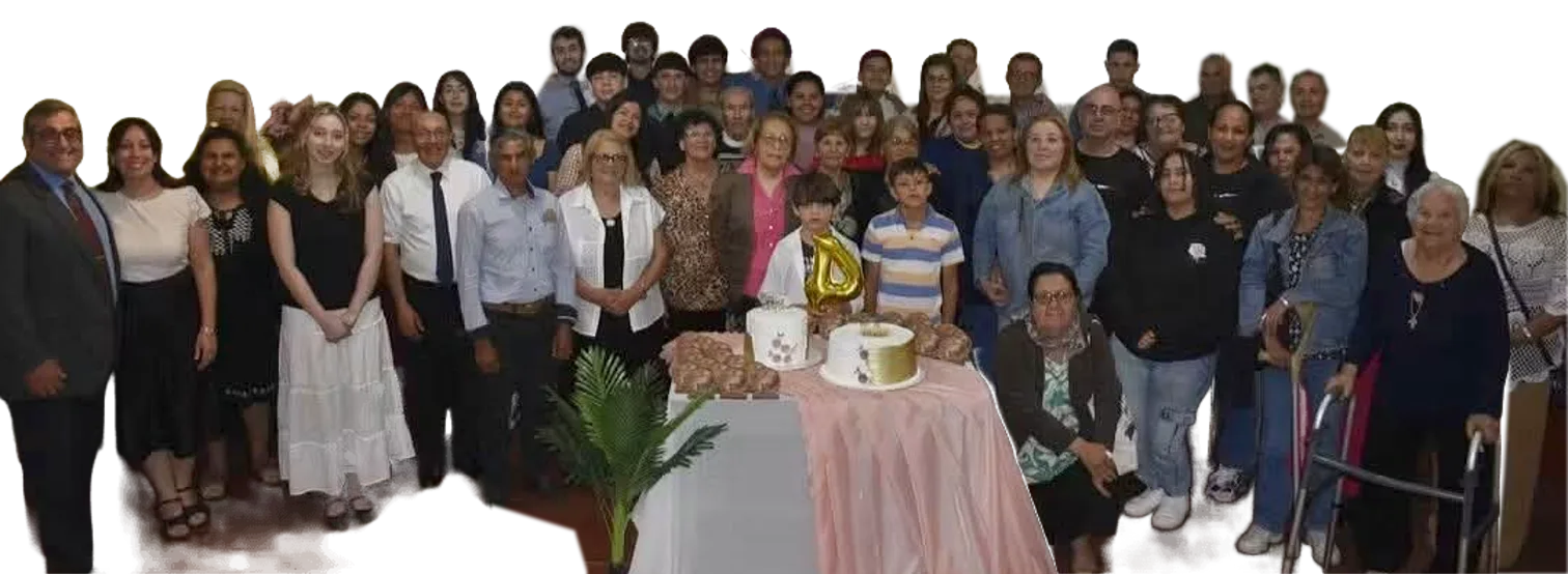 La congregación reunida en el salón de la iglesia, de pie alrededor de una mesa con tortas.